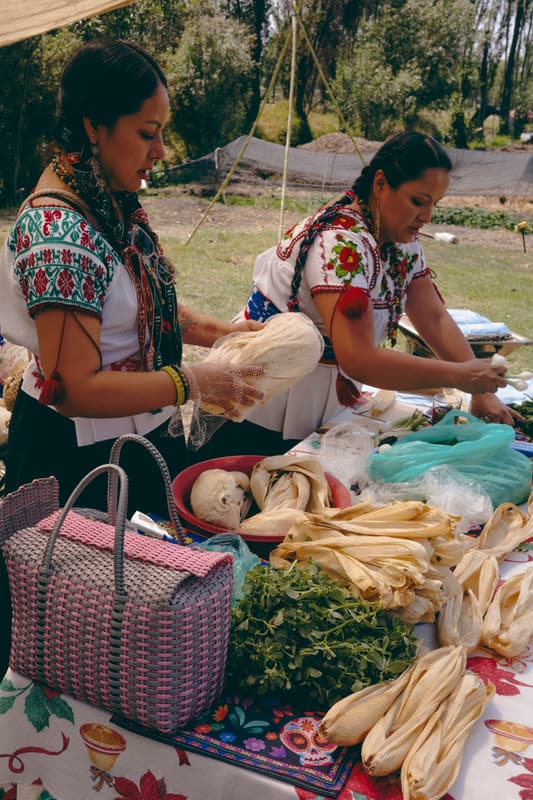 Two women in embroidered blouses preparing food at a market table