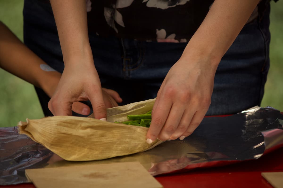 Hands wrapping a tamal in a corn husk