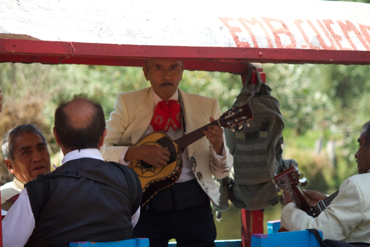 A mariachi playing guitar for guests aboard a trajinera