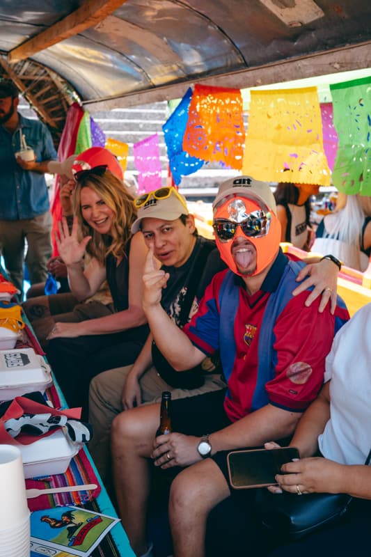 Guests waving from a trajinera strung with papel picado