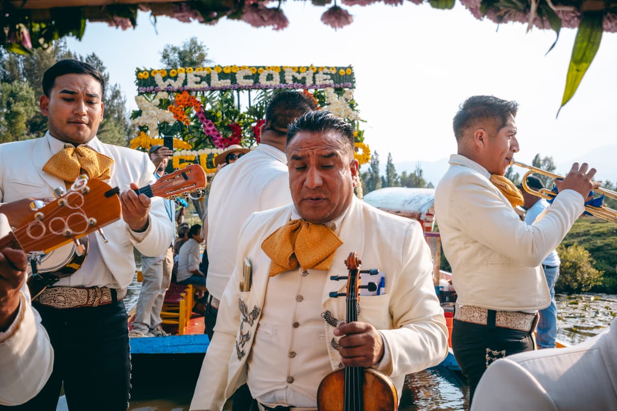 A mariachi violinist in a white charro suit beside the welcome sign