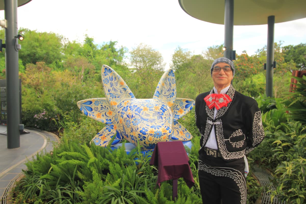 A mariachi musician in a charro suit beside the sculpture