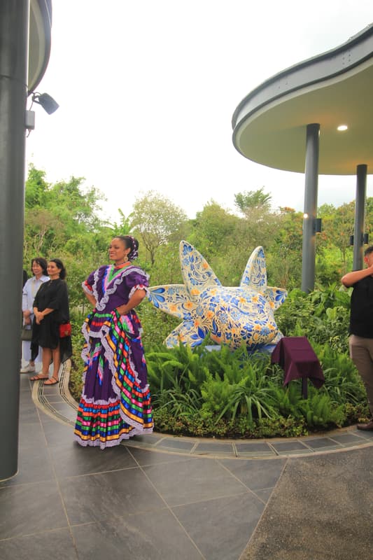 A dancer in white beside the sculpture