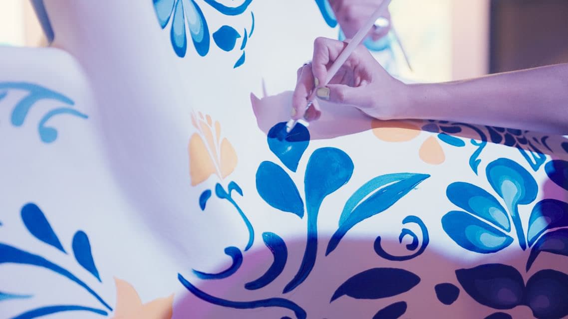 A hand painting blue floral detail onto the white sculpture